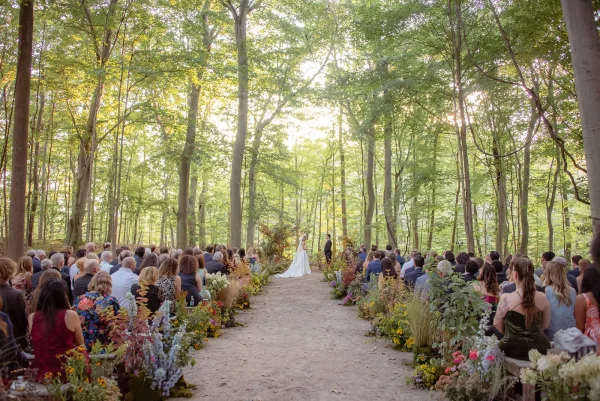 Outdoor wedding ceremony with a forest wedding ceremony aisle lined with wildflower arrangements as the bride and groom face guests on wooden benches