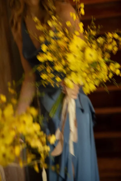 Bridesmaid portrait in a blue bridesmaid dress holding a yellow floral bouquet with ribbon tie in a dark indoor setting