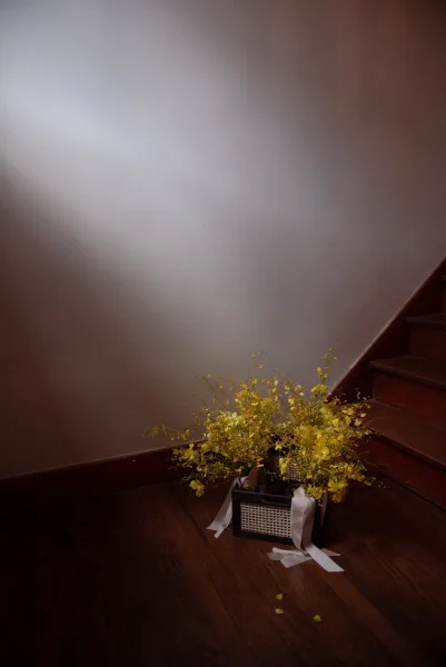 Wedding floral arrangement with yellow wedding flowers and greenery in a woven basket with ribbon beside a wood staircase indoors