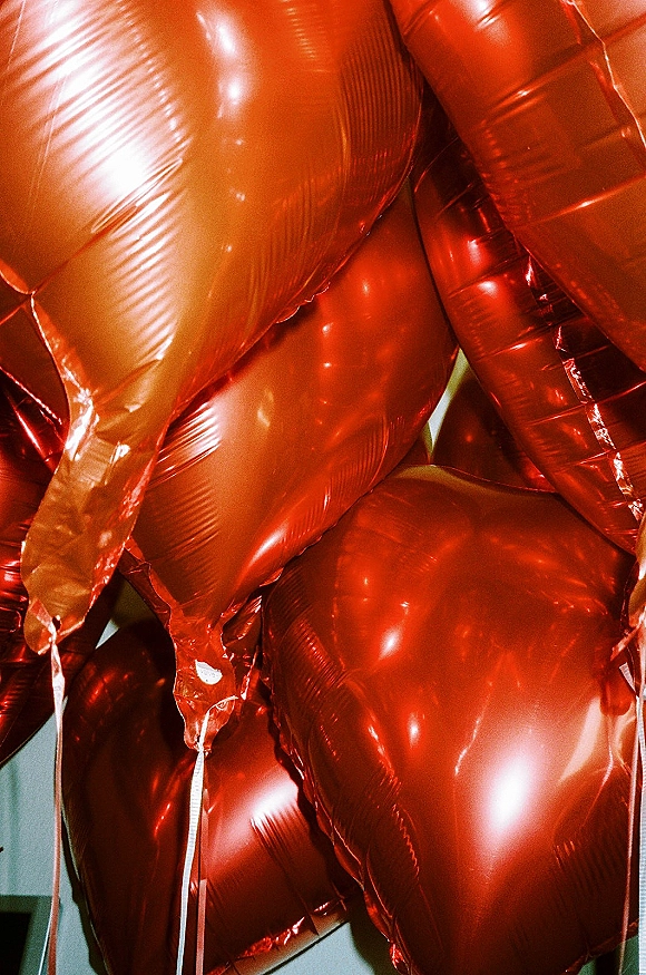 Heart balloons in shiny red heart balloons cluster with dangling strings, floating against an indoor wall backdrop for romantic decor