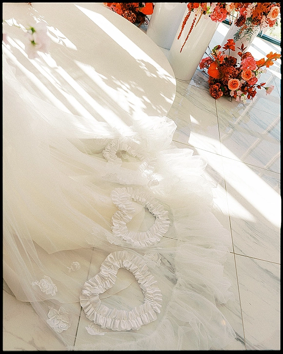 Wedding dress detail with tulle wedding dress skirt and floral lace appliqués, styled on marble tile floor in window light with shadows