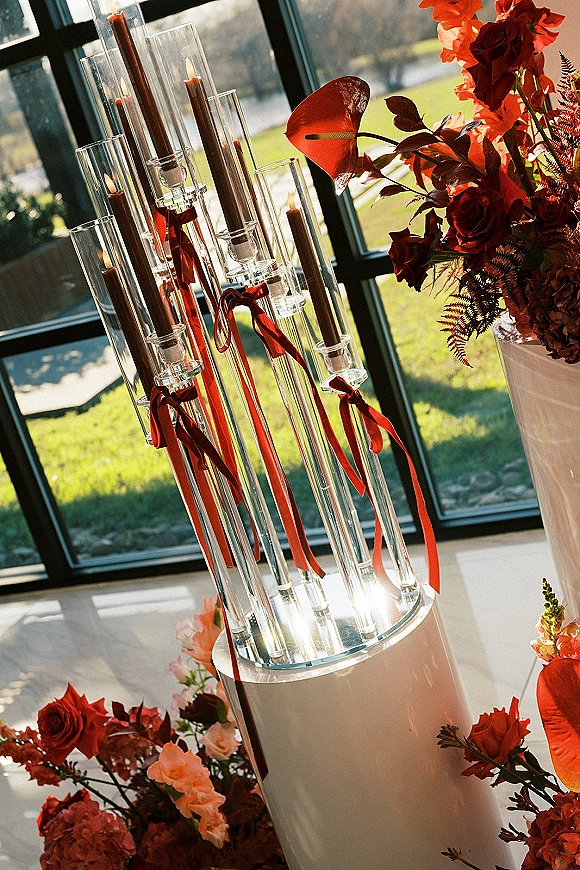 Wedding centerpiece with tall candle centerpiece glass cylinders, taper candles, red ribbons, and roses on a pedestal by sunlit windows
