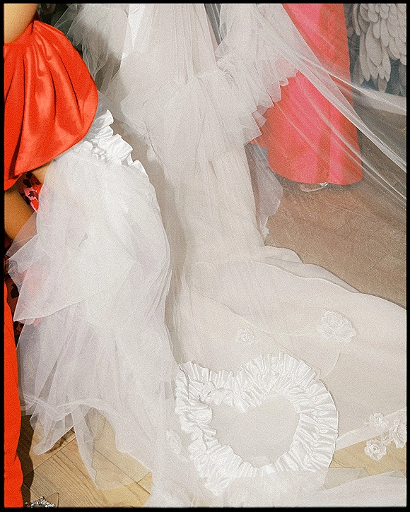 Wedding dress train with tulle wedding train cascading beside a coral bridesmaid dress on a wood floor under a wall mural