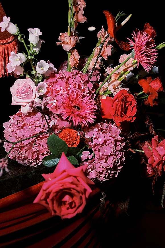 Wedding bouquet with pink and red bridal bouquet blooms, featuring roses, hydrangea, gerbera daisies, and greenery against black fabric backdrop