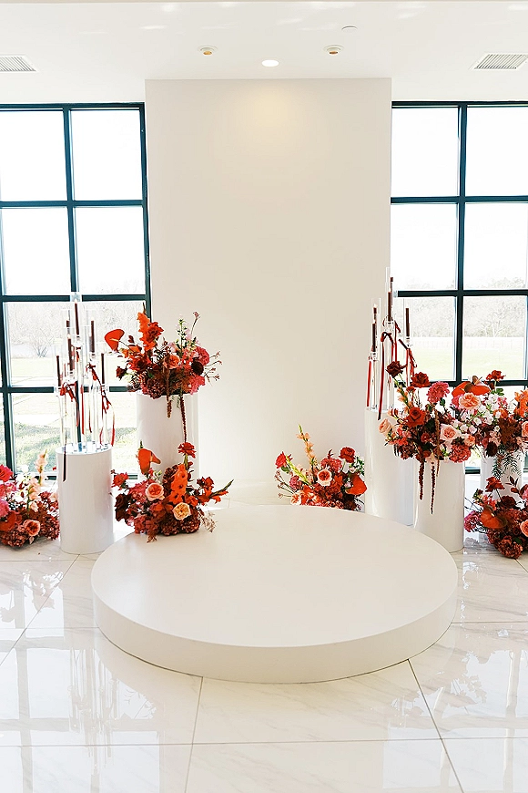 Wedding ceremony backdrop with modern ceremony backdrop styling, white plinths, clear candle cylinders, red ribbons and florals by grid windows