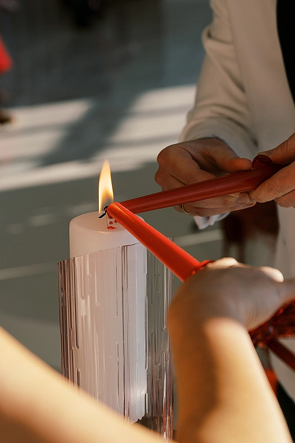 Unity candle lighting as hands in a suit jacket light a white pillar candle between tapers on a ceremony table in soft indoor light
