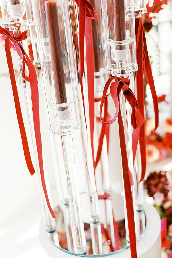 Wedding candle centerpiece with tall glass candle holders, taper candles, and red ribbon bows on a mirrored base at reception table