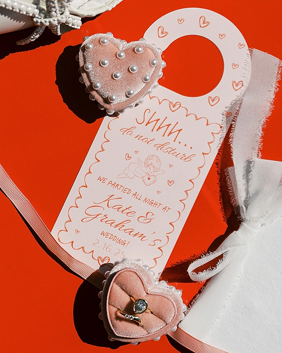 Wedding invitation suite wedding flat lay with ring box, engagement ring and band, pearl details, ribbon bow, and lace on red surface