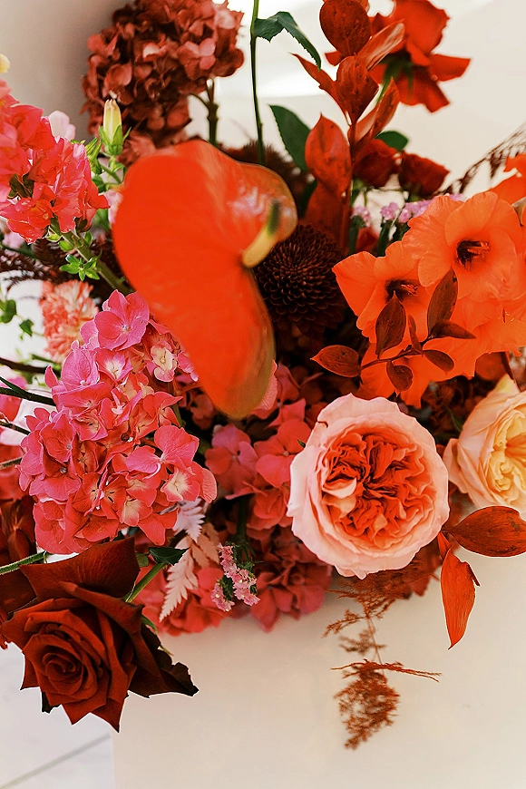 Wedding bouquet with coral tones featuring roses, hydrangea and calla lily with greenery and dried foliage on a white surface