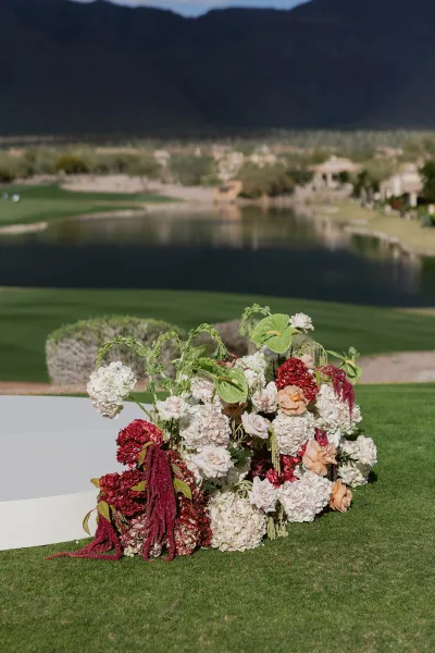 Ceremony aisle decor with wedding aisle flowers, lush hydrangeas and roses around a white runner on a lawn with pond and mountains beyond