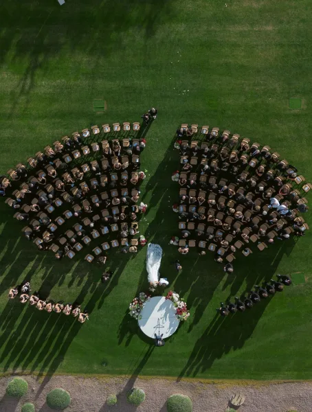 Outdoor wedding ceremony from an aerial wedding ceremony photo, showing curved seating around a circular platform with floral arrangements on a lawn