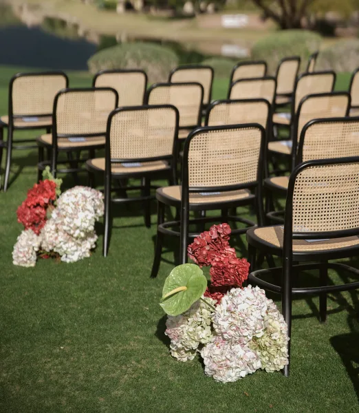 Ceremony seating with outdoor ceremony chairs mixing black and cane-back styles, lined along a floral aisle on a manicured garden lawn