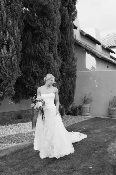 Bridal portrait in black and white of a bride looking down, holding a white rose bouquet, wearing a strapless lace dress on a garden lawn