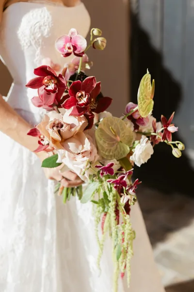 Bridal bouquet with orchid wedding bouquet of burgundy orchids, blush blooms and green anthurium, held against a strapless lace bodice by doorway shadows