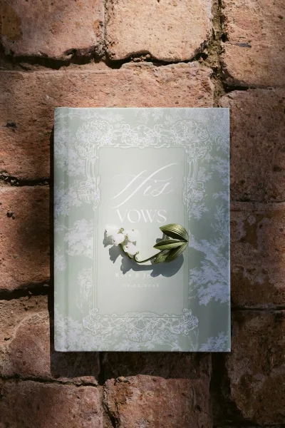 Vow book wedding vow booklets with an embossed floral cover and ribbon bookmark, styled on a brick wall background