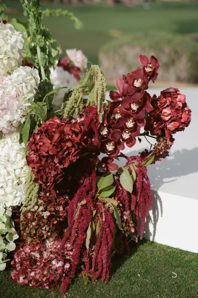 Wedding floral arrangement with hydrangeas and orchids cascading with hanging amaranthus on a white pedestal on a garden lawn
