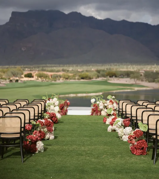 Ceremony aisle design with floral lined wedding aisle of hydrangeas and anthurium beside a grass runner, lakeside with mountain views under clouds