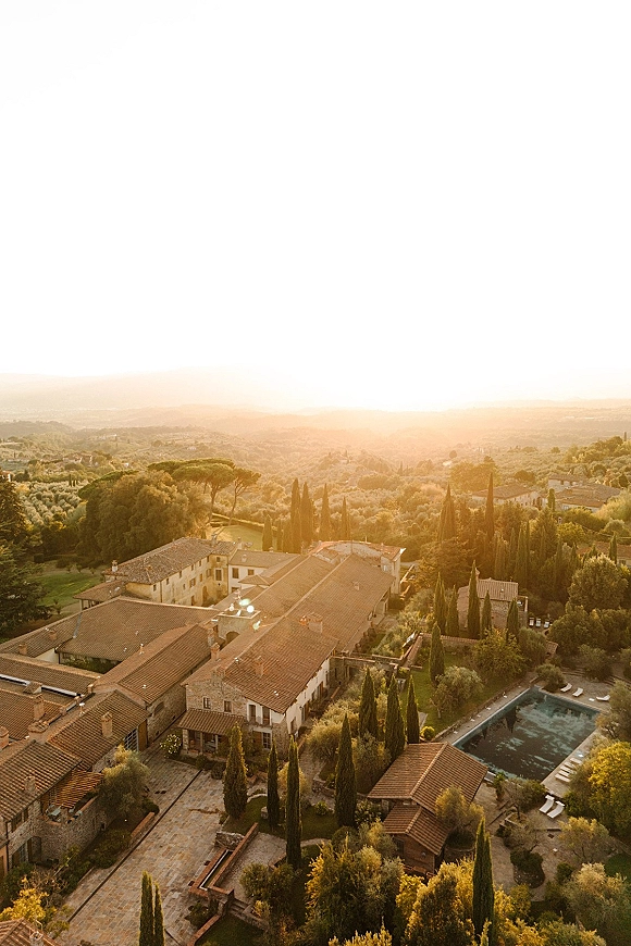Wedding venue aerial view of a stone villa wedding venue with terracotta roof, courtyard and pool, framed by cypress trees at sunset