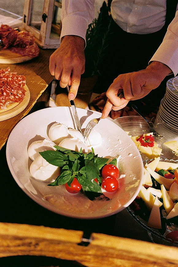 Wedding cocktail hour food displayed on a wedding charcuterie board with burrata, basil, tomatoes, salami, and cheese on a wooden table