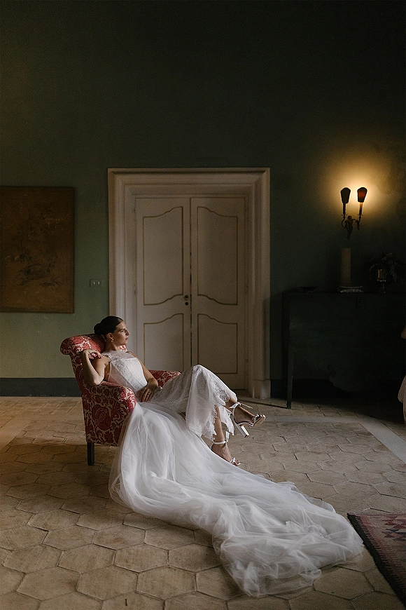 Bridal portrait of a bride sitting in chair, her tulle wedding dress train flowing across a tiled floor in a green-walled room with paneled doors