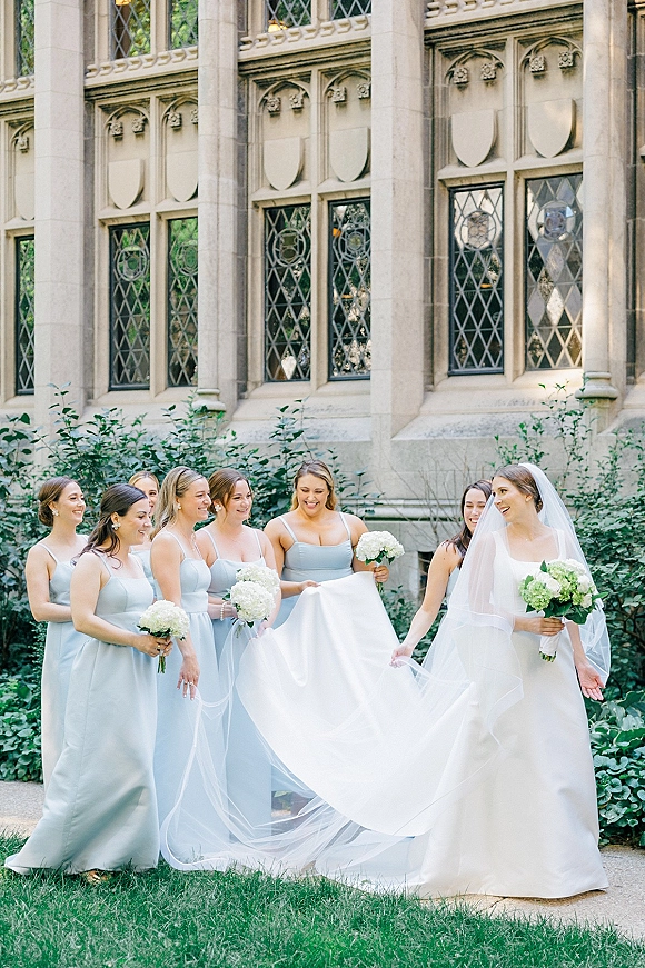 Bridesmaid group photo with bride with bridesmaids holding white hydrangea bouquets on a lawn by a stone building and leaded windows