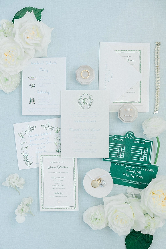 Invitation suite wedding invitation flat lay with wax-sealed envelope, rings and pearl bracelet beside white roses on light blue fabric backdrop