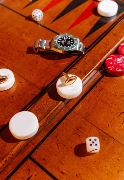 Groom accessories flatlay with wedding cufflinks detail, wristwatch, and dice arranged on a wood backgammon board with gold accents