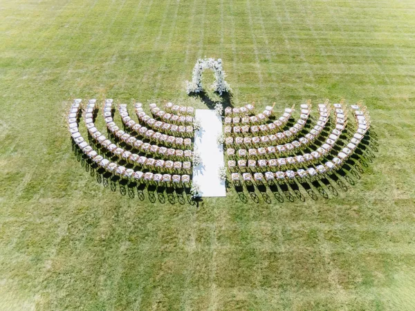 Ceremony setup with outdoor ceremony seating in the round, featuring a white aisle runner leading to a floral arch on a grass lawn