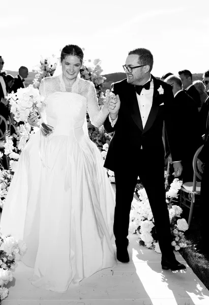 Wedding recessional bride and groom walking aisle hand in hand, bride with bouquet and veil, tuxedo groom, guests and hills behind
