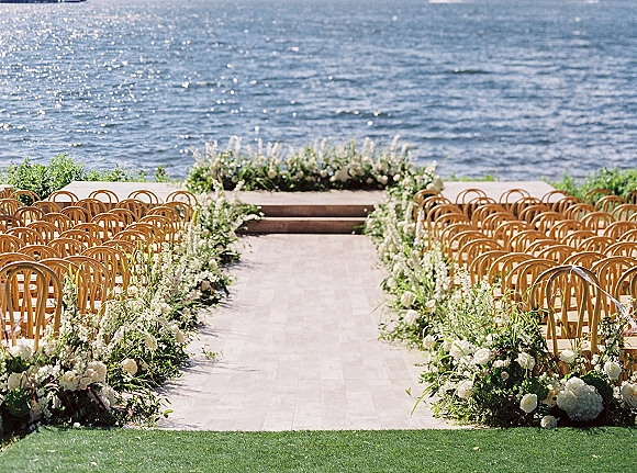 Ceremony aisle decor with outdoor ceremony aisle flowers, white roses and hydrangeas, greenery garlands and wood chairs by the oceanfront lawn