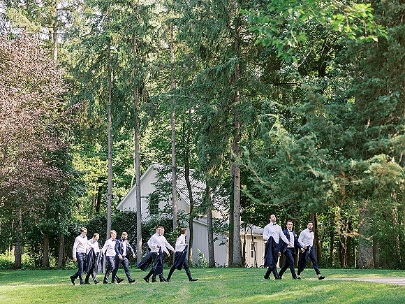 Groomsmen portrait of the wedding party men walking on a tree-lined pathway in suits with bow ties and dress shoes, candid and relaxed