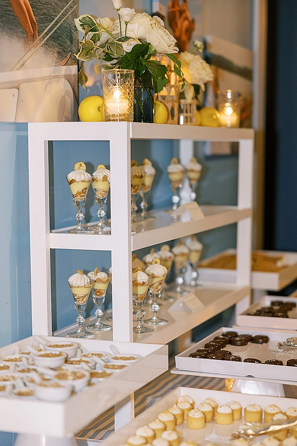 Wedding dessert table with dessert table display shelves holding mini cups, cupcakes, and truffles, styled with candles and lemons indoors