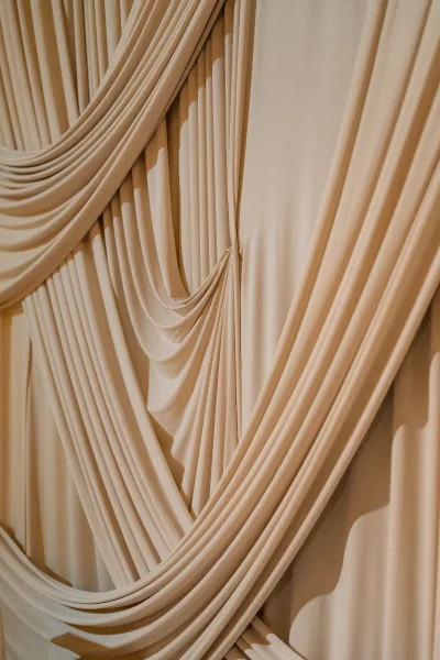 Wedding draped backdrop with wedding fabric backdrop in pleated ivory panels and gathered swags against a neutral wall in warm indoor light