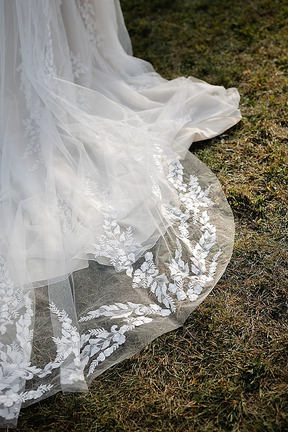 Wedding dress train with lace wedding dress train detail, scalloped hem and floral embroidery trailing over a green grass lawn