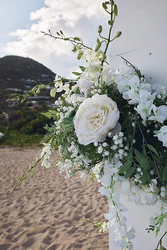 Wedding floral arrangement with white wedding flowers, peonies and orchids with baby's breath and fern greenery against a beachside wall