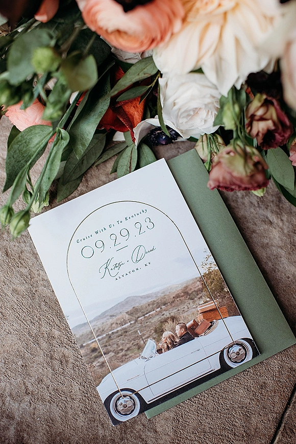Wedding invitation suite with arched wedding invitation on stone surface, styled with rose and greenery accents, vellum wrap and liner