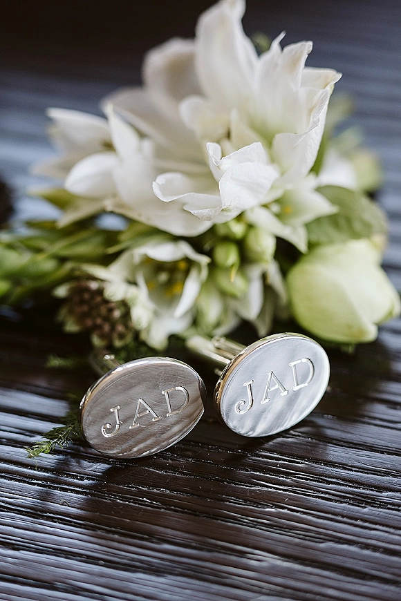 Wedding cufflinks personalized cufflinks with engraved initials beside a white boutonniere and greenery on a dark wood table