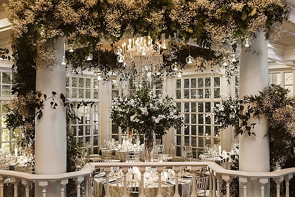 Reception tablescape with wedding reception decor, tall floral centerpieces and candlelit candelabras under chandeliers in a windowed conservatory