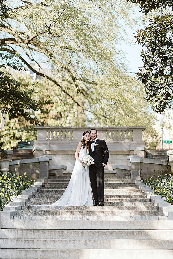 Couple portrait of bride and groom portrait hugging on a stone staircase, bride holding a white bouquet with veil and groom in tuxedo