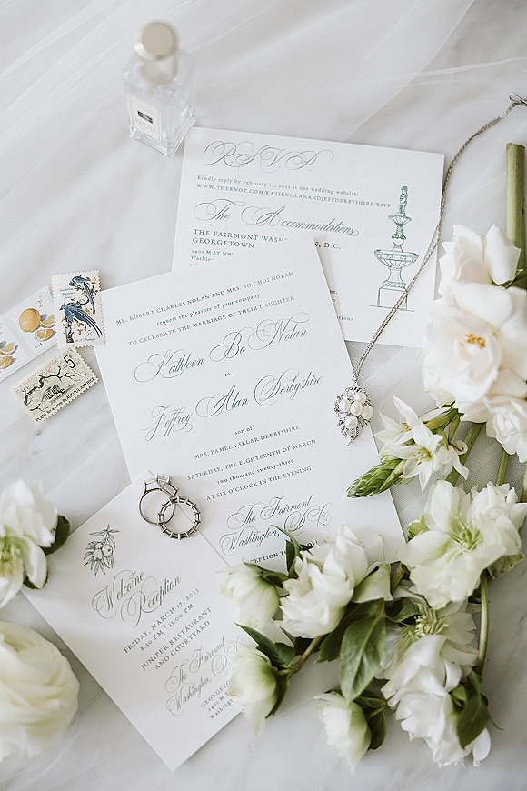 Invitation suite with letterpress wedding invitations, RSVP and envelopes, vintage postage, rings, pearl pendant and perfume on white fabric backdrop