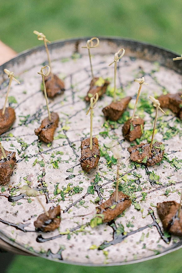 Wedding appetizers on a serving tray, passed hors doeuvres of bite-size beef cocktail skewers with herbs and balsamic glaze outdoors