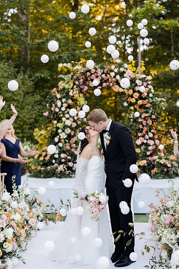 Wedding kiss portrait of bride and groom kissing under a floral arch as bubbles float around them at an outdoor garden ceremony