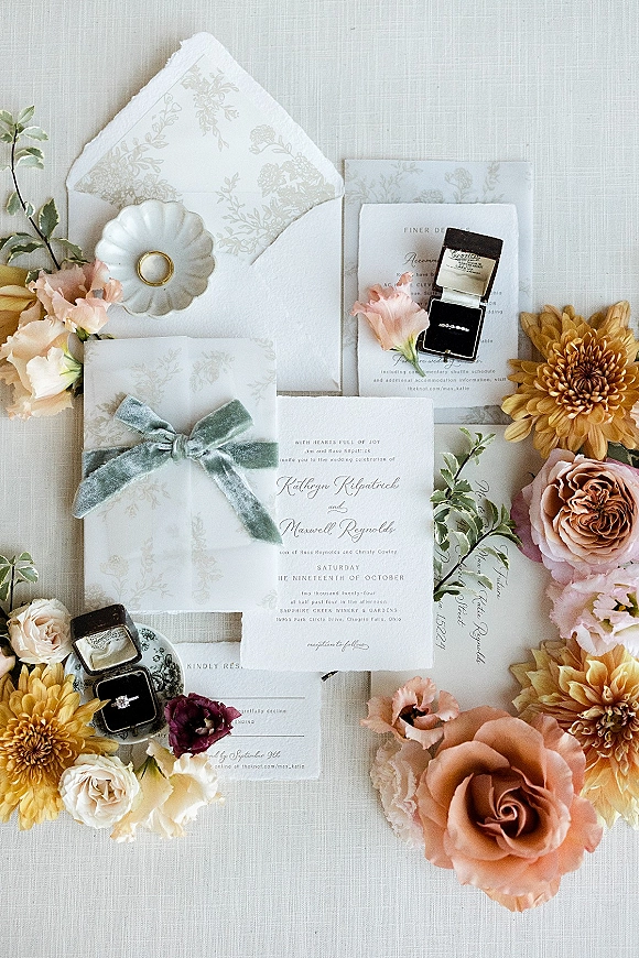 Wedding invitation suite with deckle edge wedding invitations, vellum wrap, velvet ribbon bow, wax seal, and flowers on neutral linen flat lay
