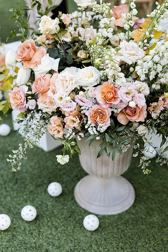 Wedding floral arrangement in a pedestal urn vase with garden roses, lisianthus, and greenery on a lawn beside white chairs