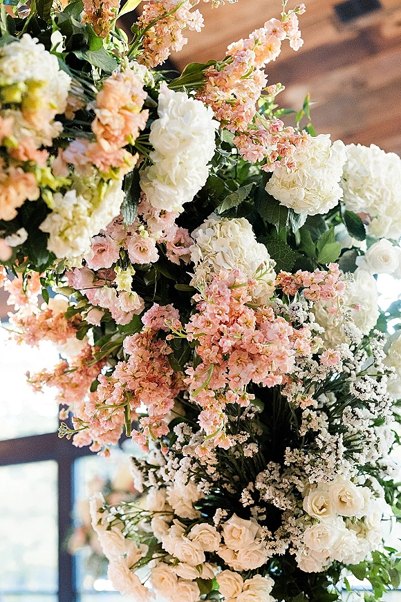 Wedding floral arrangement with white hydrangeas, roses, and pink stock, accented by baby's breath and greenery in an indoor venue with beams