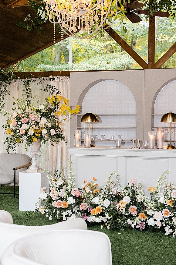Wedding bar setup with wedding bar backdrop panels, candlelit counter, greenery garland, and chandelier under a draped wood pavilion