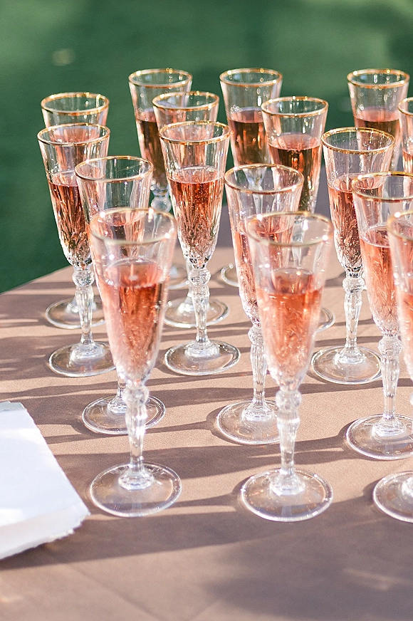 Champagne toast setup with wedding champagne toast flutes filled with sparkling rosé lined on crisp table linen in sunlit lawn setting
