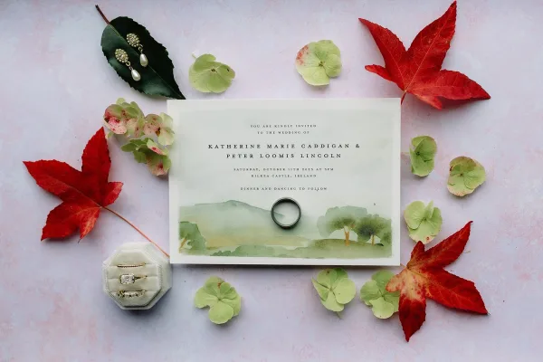 Wedding invitation suite with watercolor wedding invitation, engagement ring in velvet box and pearl drop earrings on a light pink flat lay background