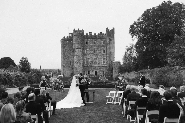 Ceremony moment at a castle wedding ceremony as bride and groom kiss at the altar, veil flowing, guests seated on lawn chairs behind