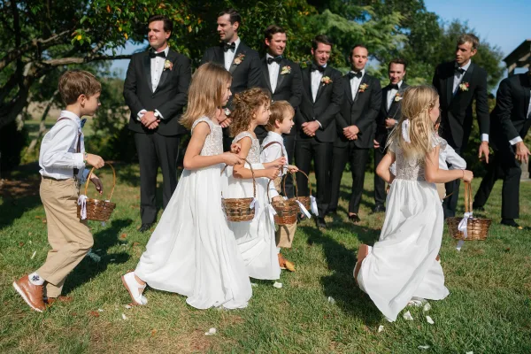 Flower girl procession during an outdoor ceremony processional, little attendants scattering flower petals down the aisle.
